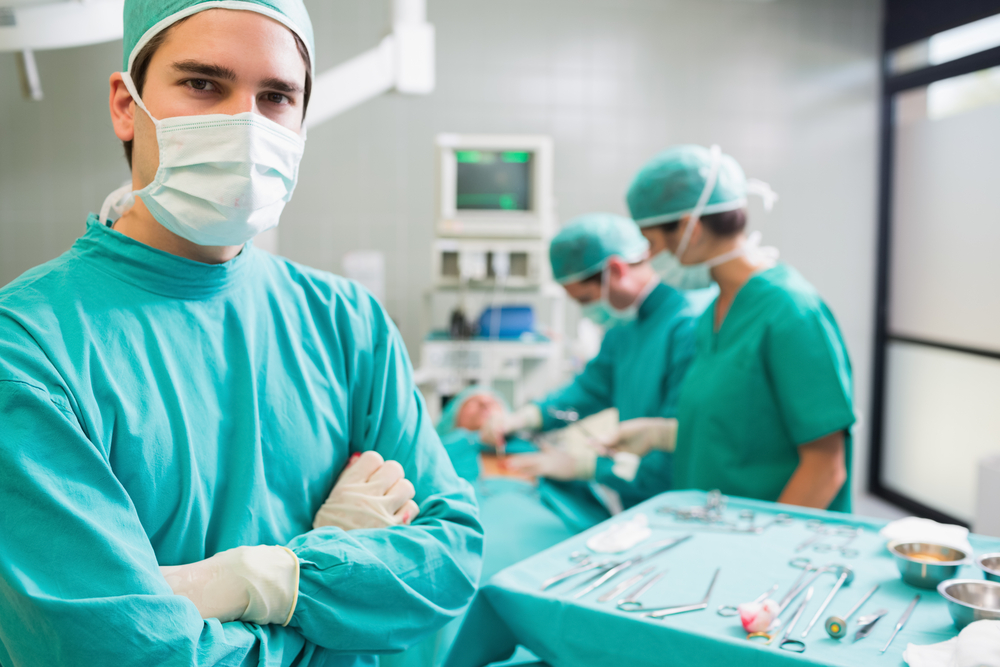 Surgeon with arms crossed looking at camera with colleagues performing in background